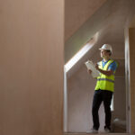 Man in hard hat and high vis jacket inspecting a recently plastered new build
