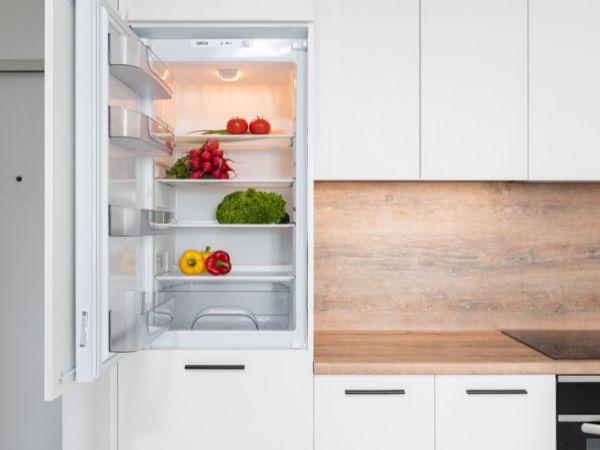 Fridge freezer open with fruit and vegetables on the shelves