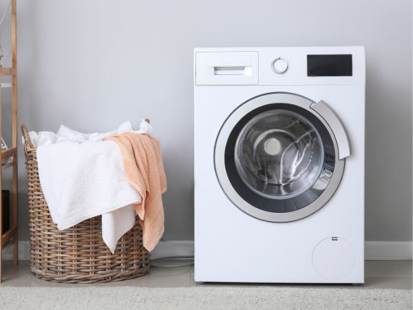White washing machine with a laundry basket next to it